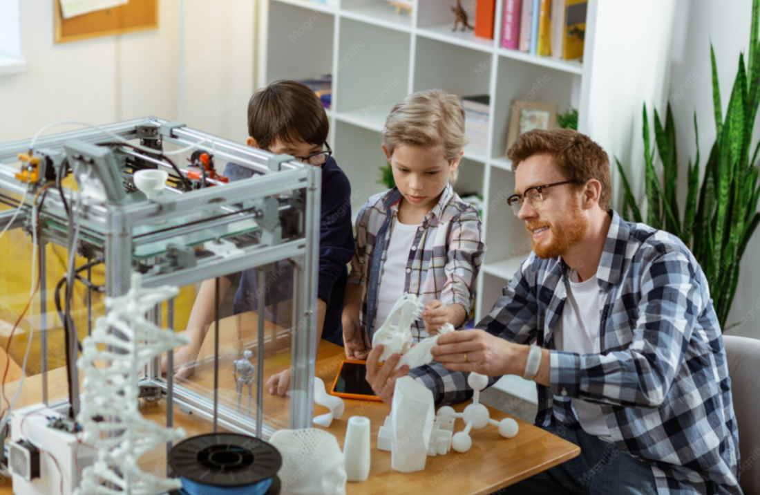 An instructor sits with two children at a table, examining white 3D-printed models beside a large 3D printer. The group appears engaged in a hands-on STEM learning activity in a bright classroom with bookshelves and plants in the background.